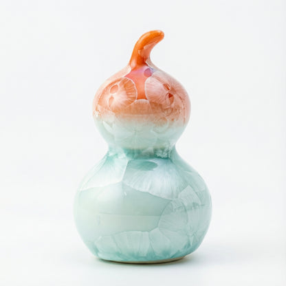 A small ceramic gourd with a vibrant coral orange and white crystalline glaze.