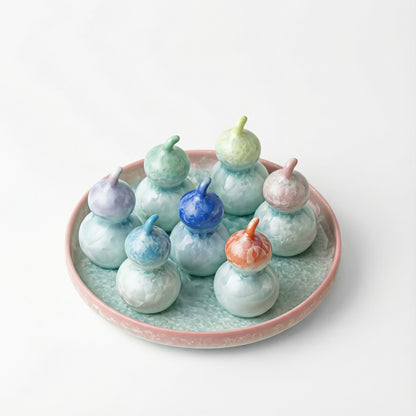 A collection of seven small ceramic gourds arranged on a plate, featuring crystalline glazes in rainbow colors including blue, orange, pink, green, and purple.